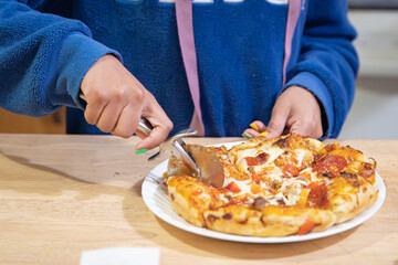 Child cutting homemade pan pizza with a rotary cutter