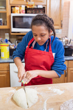 Child cutting a fresh ball of dough in half with a knife.