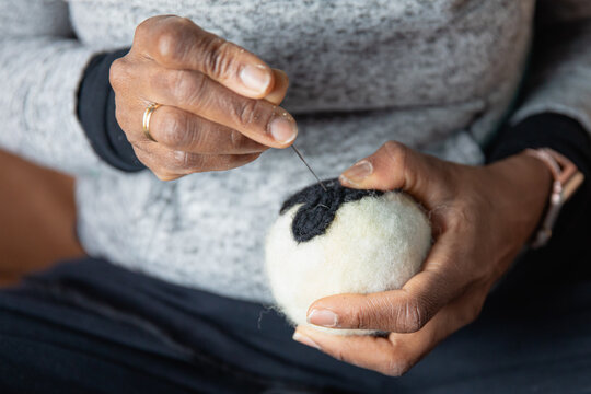 Hands using a needle to felt cute designs onto handmade dryer balls