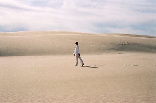 Woman walking across sandy desert landscape with sun hat.