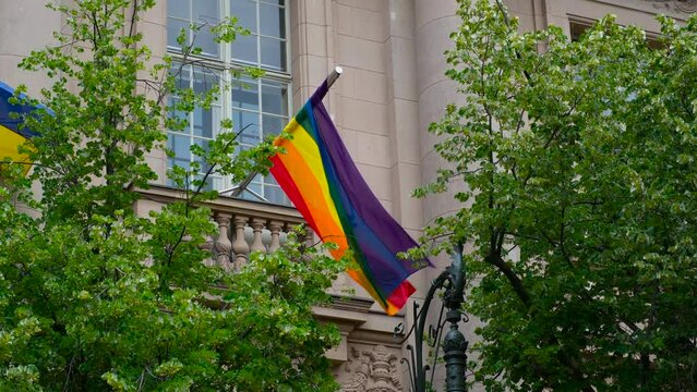 Flag of the LGBT community. The rainbow flag is installed on the balcony of the building and flutters in the wind among the trees. LGBT minority flag.