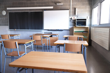 Empty high school classroom with natural light. Wooden desks and chairs, blackboard and whiteboard. Education.