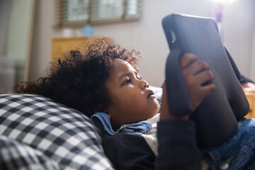 Close up of little boy lying on bed using digital tablet at home