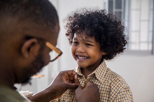 Father getting his little cheerful son ready, buttoning school shirt