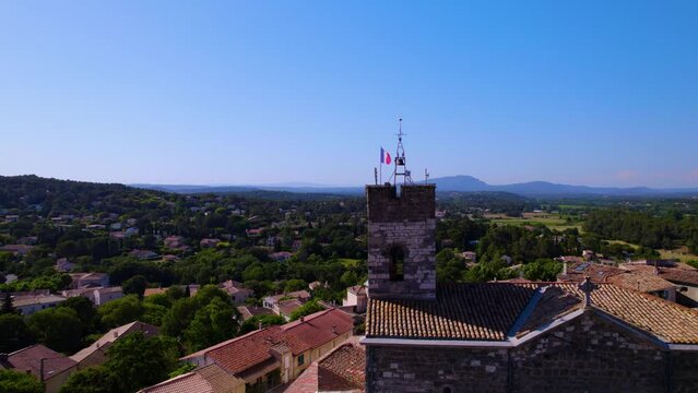 Picturesque Village Scene: Church Bell Tower with French Flag Amidst the South of France, Pic St Loup Mountains in the Background