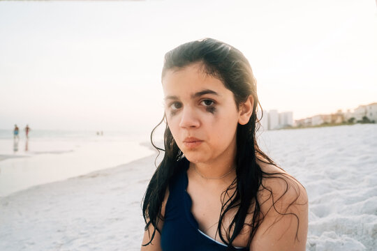 A preteen girl making silly faces, sitting on the beach. 