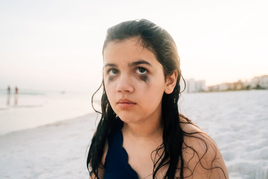 A girl sitting on the beach, unhappy to have her picture taken. 