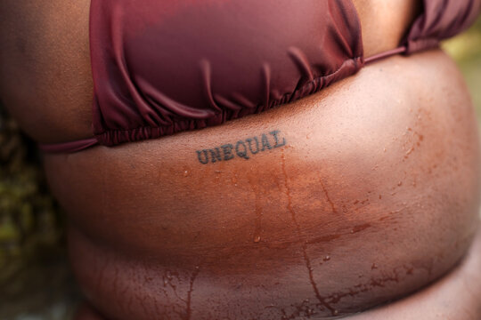 Tattoo that says Unequal over black skin