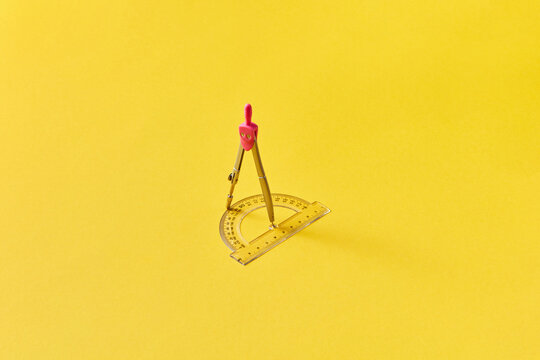 Pink compass and protractor on bright yellow background.