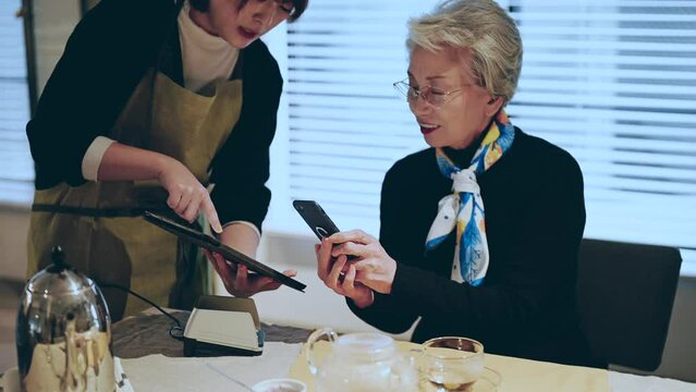 顧客のシニア女性にタッチレス決済を案内するカフェ店員