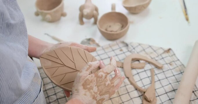 woman creates pattern on a leaf shaped piece of clay by hands in artistic studio