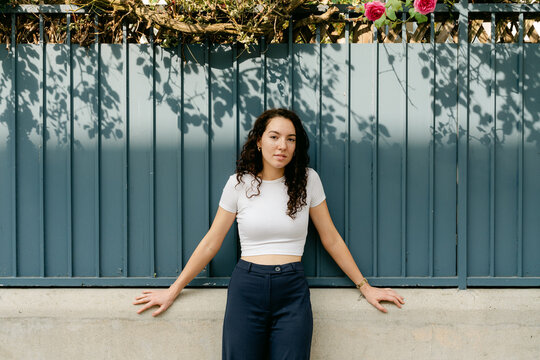 portrait of young woman with curly hair leaning on wall