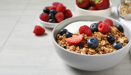 Tasty granola, yogurt and fresh berries in bowl on white tiled table, closeup with space for text....