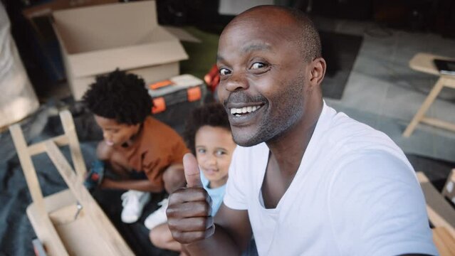 Handsome black father vlogging to camera with two mixed race sons while working on DIY project together in the garage