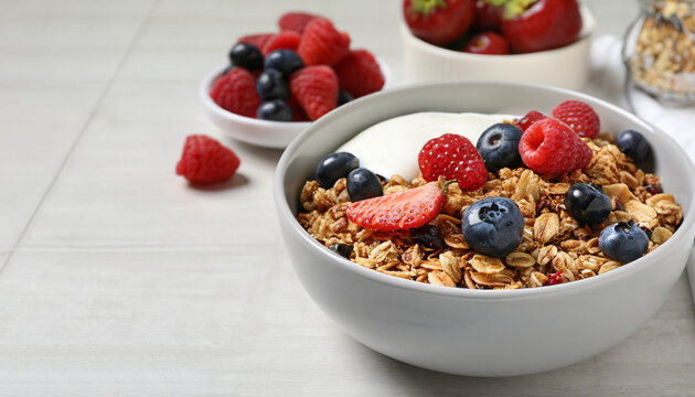 Tasty granola, yogurt and fresh berries in bowl on white tiled table, closeup with space for text. Healthy breakfast