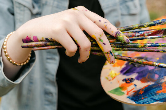 close up of hand holding paint brushes with colorful palette 