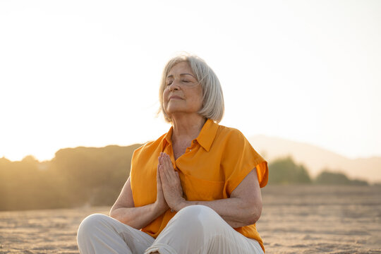 Happy retired woman at beach doing meditation