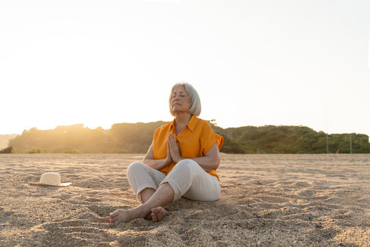 Happy retired woman at beach doing meditation