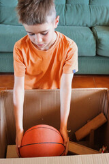 Boy in a house move picking up a basketball from a cardboard box