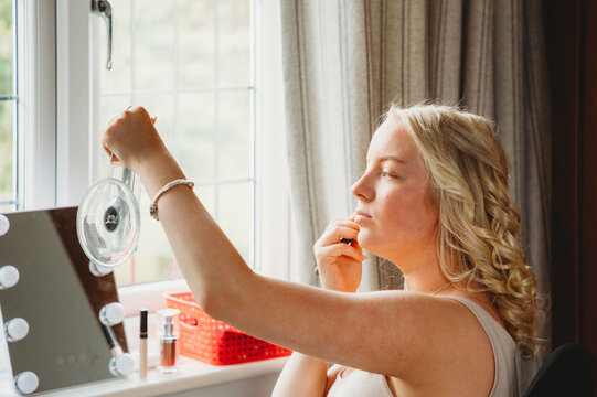 Teenage girl in her bedroom applying makeup in front of the window.