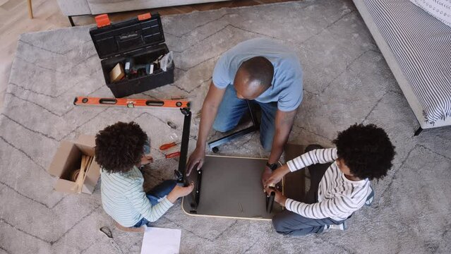 Above shot of Mixed race father and sons assembling flat pack DIY furniture and waving at camera