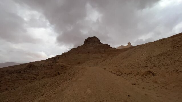Road to Ksar Guermessa troglodyte village in Tunisia on cloudy day with mosque in background