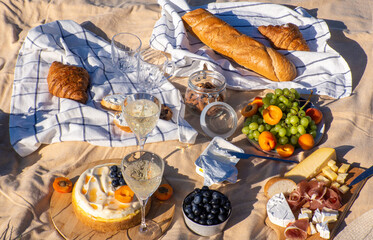 Beige blanket with fruits and pastries, cookies, berries, cheese and baguette. Concept of having picnic for two in a city park during summer holidays or weekends. Copy space. Two glasses of wine.
