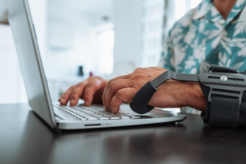 Man with adjustable articulated elbow orthosis typing on laptop keyboard