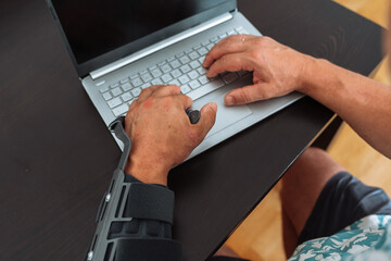 Man with adjustable articulated elbow orthosis typing on laptop keyboard