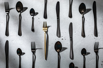 A golden fork among black flatware. Neutral gray concrete background