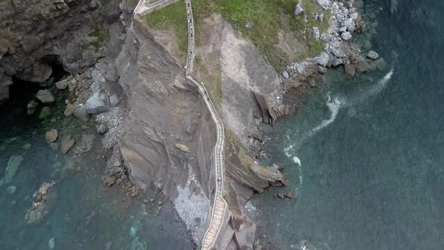 Aerial descend pan up to monastery stairway on Gaztelugatxe Basque Spain, cloudy day at sea