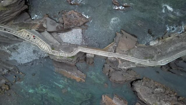 Stairway path leading to Gaztelugatxe island in rocky ocean, ascending bird's eye view, Basque Spain