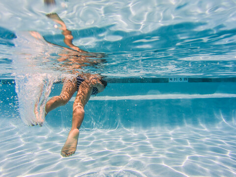 Girl in blue striped swimsuit swimming away at public pool