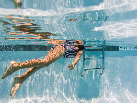 Girl in blue striped swimsuit swimming at public pool