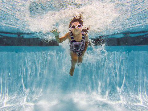 Girl in striped swimsuit jumping into public pool