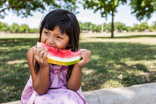Girl sitting on curb biting a watermelon