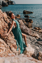 Woman green dress sea. Woman in a long mint dress posing on a beach with rocks on sunny day. Girl on the nature on blue sky background.