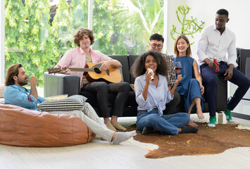 Happy multiethnic friends having party at home. Caucasian man playing acoustic guitar while sitting...