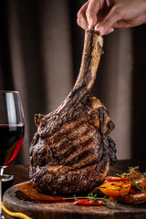 The chef holds a large piece of roasted meat on the bone, tomahawk, lamb or veal.