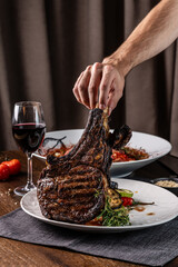 The chef holds a large piece of roasted meat on the bone, tomahawk, lamb or veal.