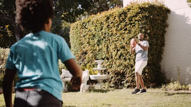Black father and son throwing the football in the garden