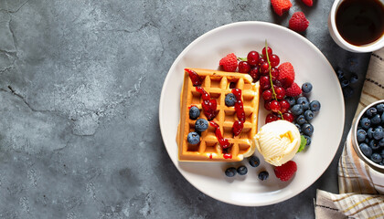 Waffles with ice cream, berries and cup of coffee on concrete background. Top view with copy space for your text. Tasty breakfast