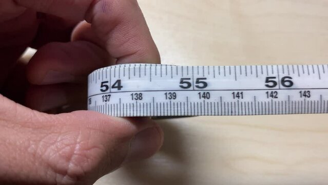 Male hands slowly pull measurement tape roll on wooden table close up shot display inch and centimeter number. Concept of weight loss, healthy lifestyle.