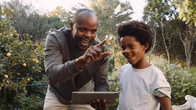 Close up of b lack father teaching son about renovation and landscaping in garden on digital tablet