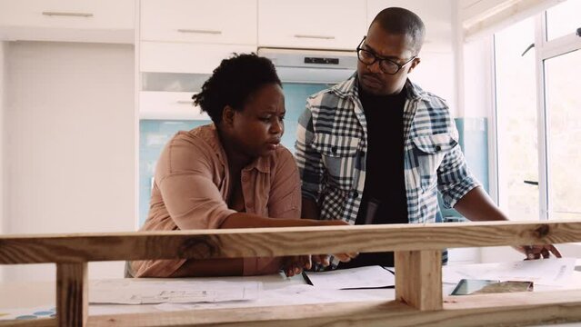 Black couple contemplating renovation plans on digital tablet and design drawings, home DIY renovation improvement