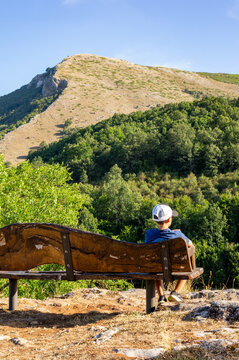Ni&ntilde;o con gorra sentado en un banco observando la monta&ntilde;a.