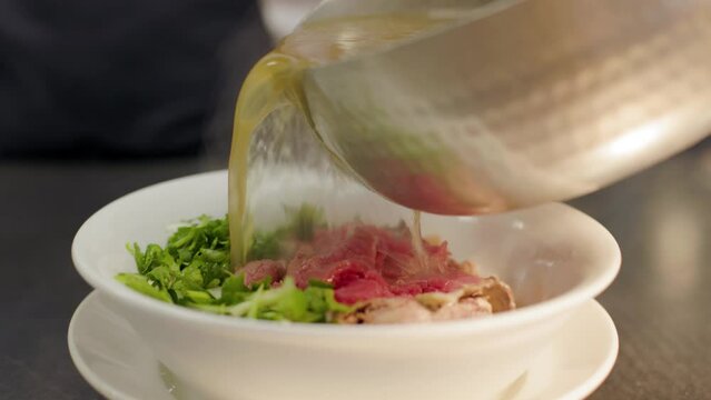Bowls of pho with broth being poured in a restaurant kitchen, beef pho, Vietnamese food. 4K 24FPS