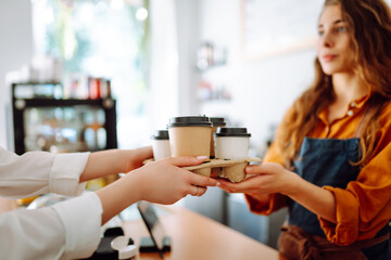 Beautiful barista woman issues coffee orders to go in a coffee shop. Small business owner. Takeaway food and drinks.