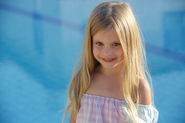 Portrait of adorable 5 years old girl with long blonde hair, blue eyes and blue swimming pool water...