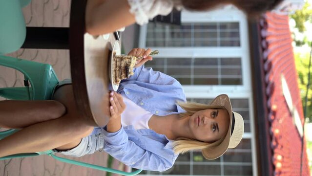 Woman is enjoying cake with her best friend in a cafe on the weekend. She is smiling and talks to her friend.